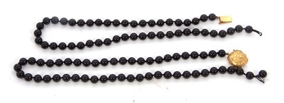 Lot 242 - A black bead necklace with gold clasp, the...
